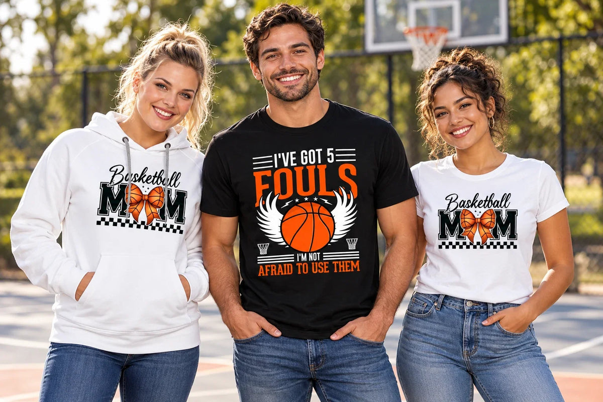 Three fans wearing Basketball shirts and a hoodie with Basketball Mom and I’ve Got 5 Fouls designs beside an outdoor court.
