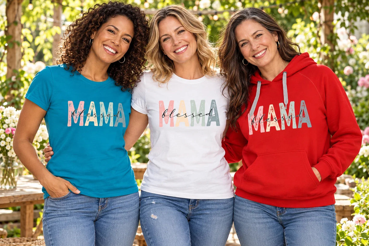 Three women wearing Blessed Mama shirts and a red hoodie with pastel retro Mama lettering in a garden.