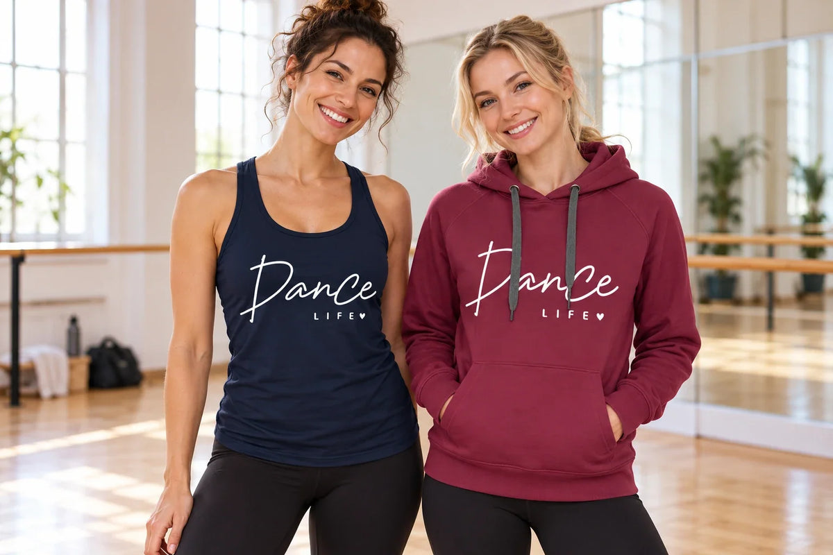 Two women wearing a navy Dance Life tank top and burgundy Dance Life hoodie in a bright dance studio.