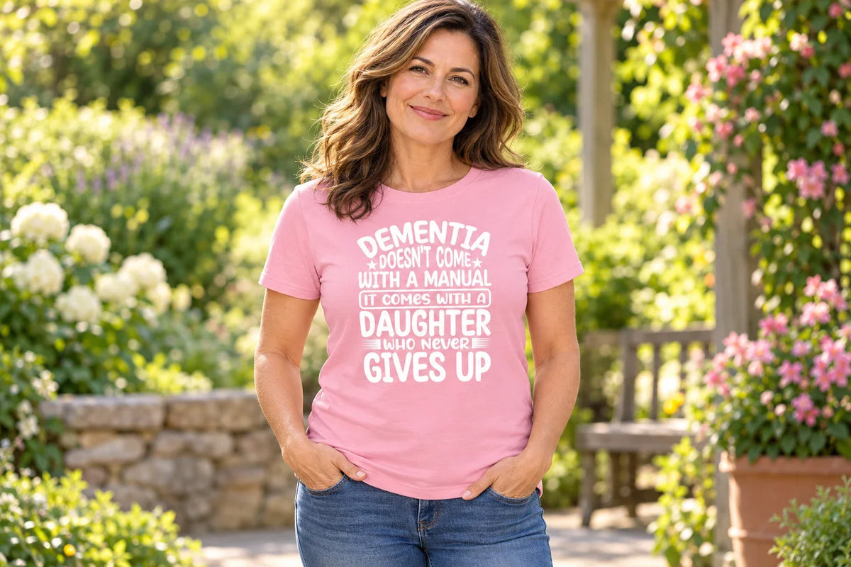 Woman wearing a pink Dementia Awareness T-shirt with the Daughter Who Never Gives Up message in a sunlit garden.